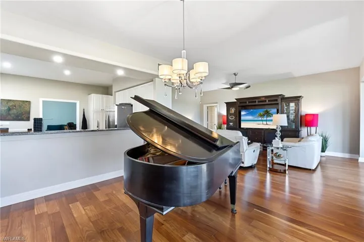 Living room with dark hardwood floors and a notable chandelier and piano