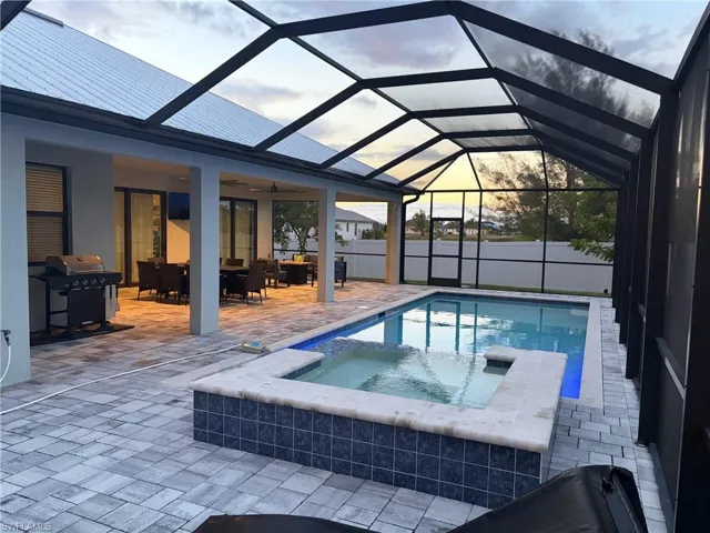 View of pool featuring a sunroom, a patio, a lanai, a pool with connected hot tub, and a grill
