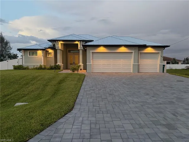 Prairie-style house featuring a metal roof, decorative driveway, stucco siding, an attached garage, and a standing seam roof