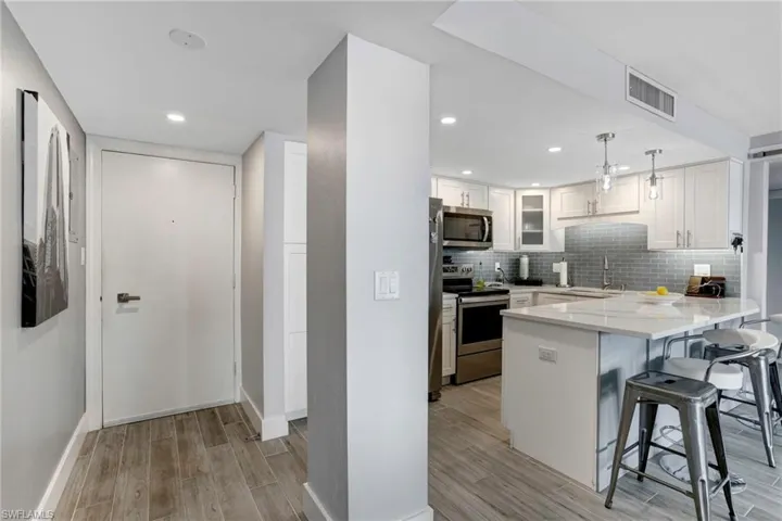 Kitchen with light stone countertops, light hardwood / wood-style flooring, hanging light fixtures, white cabinets, and appliances with stainless steel finishes