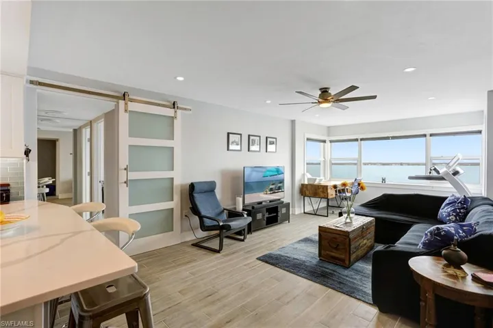 Living room with a barn door, ceiling fan, a water view, and light hardwood / wood-style flooring