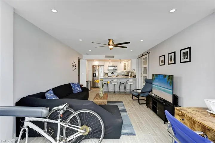 Living room with a barn door, light wood-type flooring, and ceiling fan