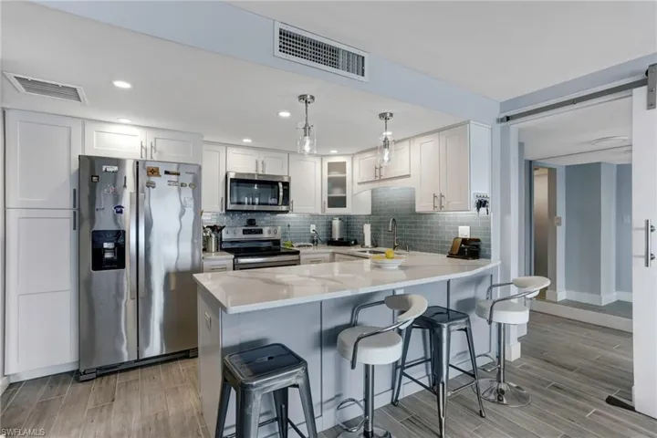 Kitchen with hanging light fixtures, light hardwood / wood-style flooring, appliances with stainless steel finishes, white cabinets, and backsplash