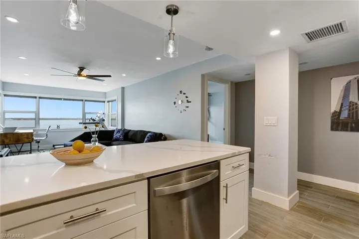 Kitchen featuring ceiling fan, dishwasher, light stone counters, hanging light fixtures, and white cabinets
