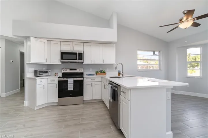 Kitchen with stainless steel appliances, a peninsula, white cabinetry, wood tiled floors, and high vaulted ceiling