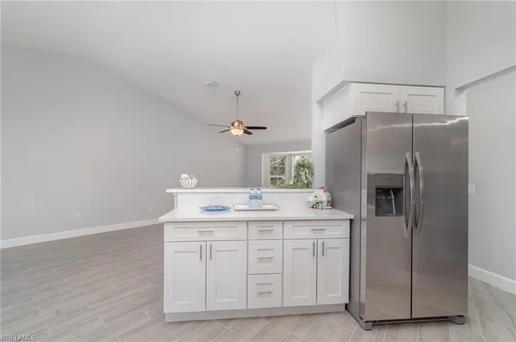 Kitchen with stainless steel fridge with ice dispenser, a peninsula, white cabinetry, vaulted ceiling, and a ceiling fan