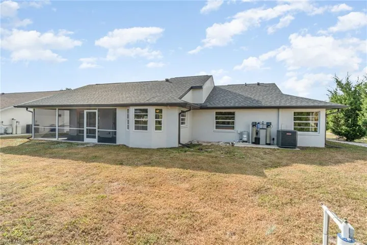 Back of property featuring a lawn, stucco siding, roof with shingles, and a sunroom