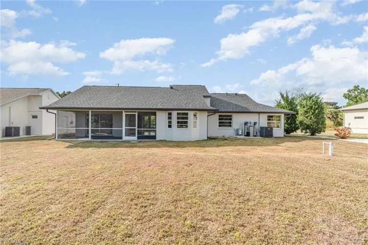 Back of property with a lawn, a sunroom, roof with shingles, and stucco siding