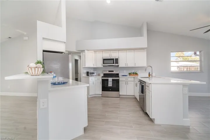 Kitchen featuring a peninsula, stainless steel appliances, lofted ceiling, white cabinets, and wood tiled floors