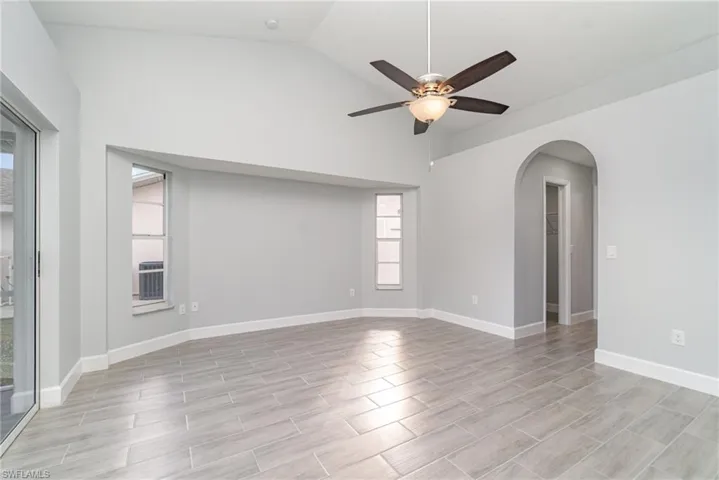 Empty room with vaulted ceiling, arched walkways, wood finish floors, and a ceiling fan