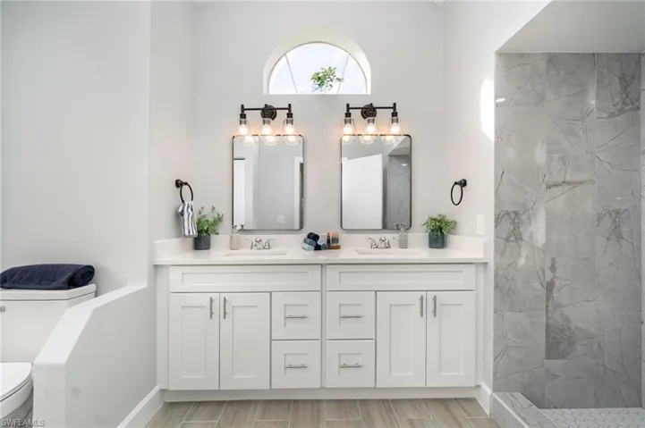Bathroom with double vanity, a marble finish shower, and wood finish floors