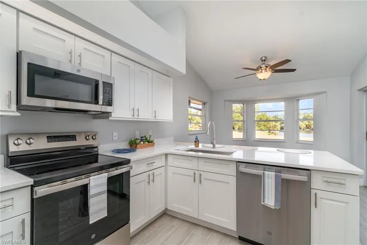 Kitchen featuring appliances with stainless steel finishes, a peninsula, white cabinets, light stone counters, and lofted ceiling