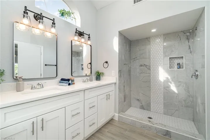 Bathroom featuring a marble finish shower, double vanity, and wood tiled floors