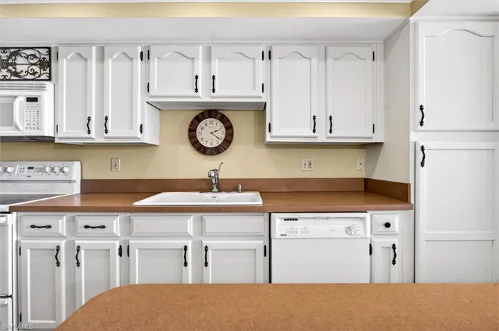 Kitchen featuring white cabinetry with dark hardware, a built-in microwave, an electric range, a stainless steel sink, a dishwasher, and brown countertops