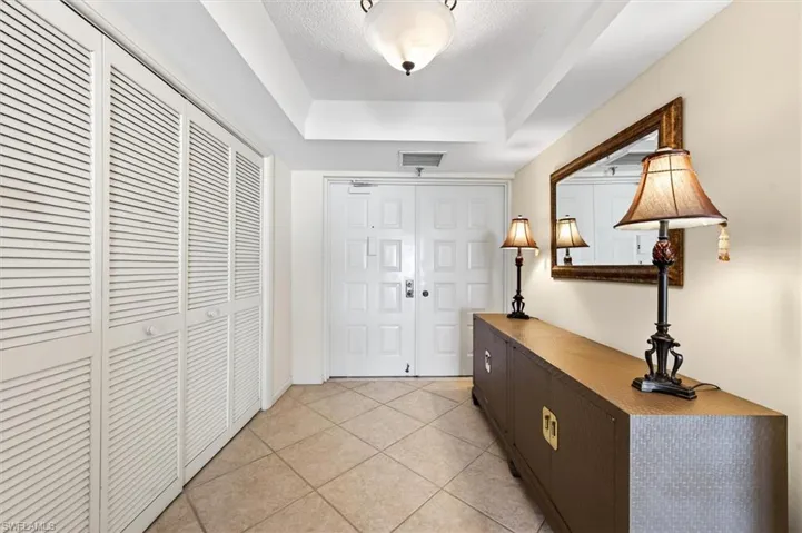 Entryway featuring neutral-toned tile flooring, louvered bi-fold closet doors, a tray ceiling, and a prominent double entry door