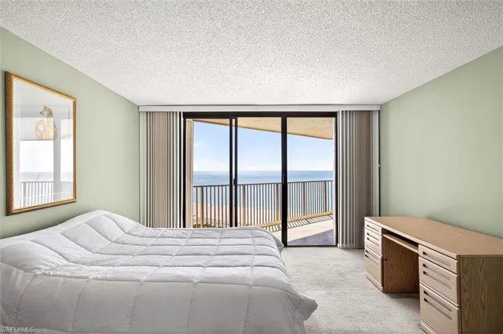 Room featuring a private balcony with ocean scenery, sliding glass doors, textured ceiling, and light-colored carpeting