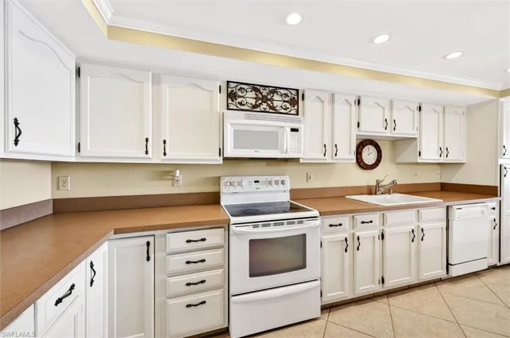 Kitchen featuring white cabinetry with dark hardware, solid surface countertops, white over-the-range microwave, built-in dishwasher, and recessed ceiling lighting