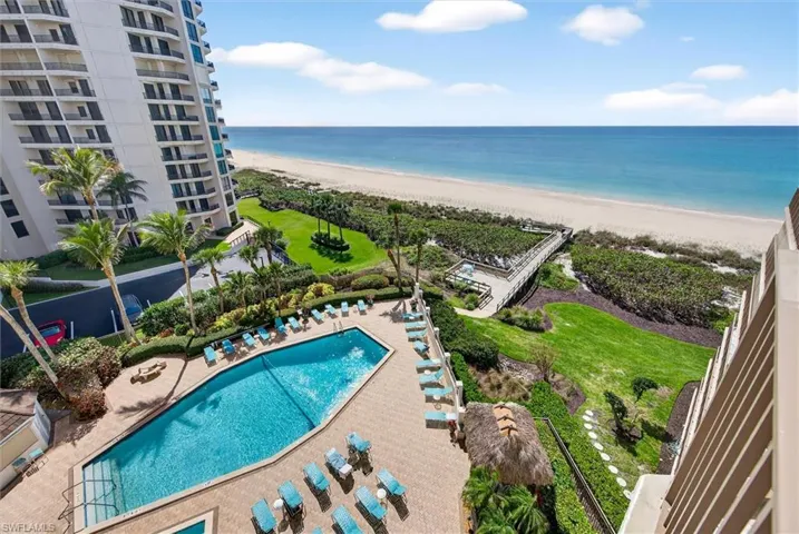 Beachfront high-rise building featuring a geometric swimming pool, extensive patio deck, and a wooden boardwalk leading to the sandy beach and ocean