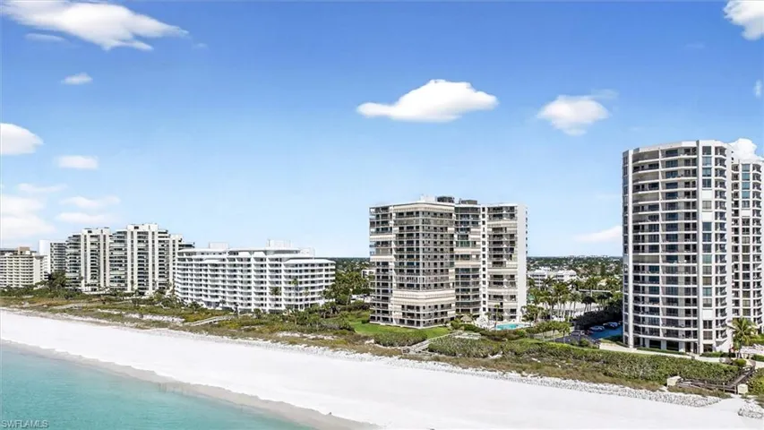 Coastal residential towers featuring private balconies and lush landscaping, positioned along a white sand beach and turquoise water