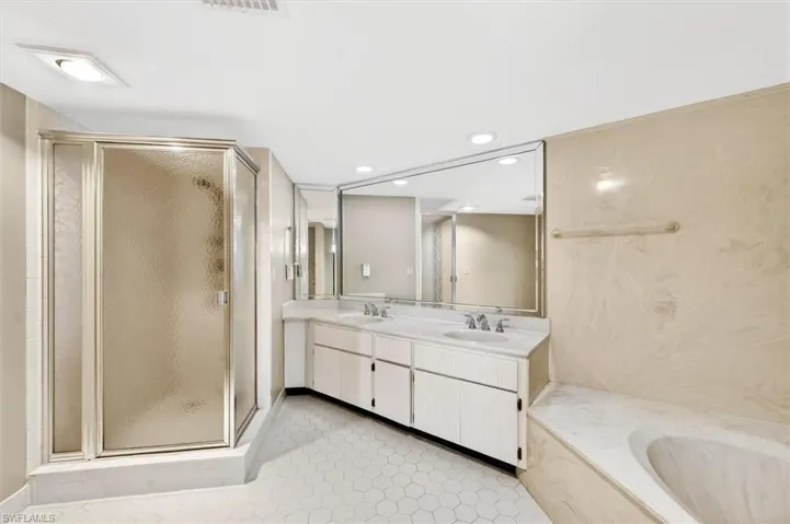 Bathroom featuring a double vanity with stone countertops, an integrated soaking tub, a stand-up shower with a textured glass door, hexagonal floor tiling, and a large wall-mounted mirror