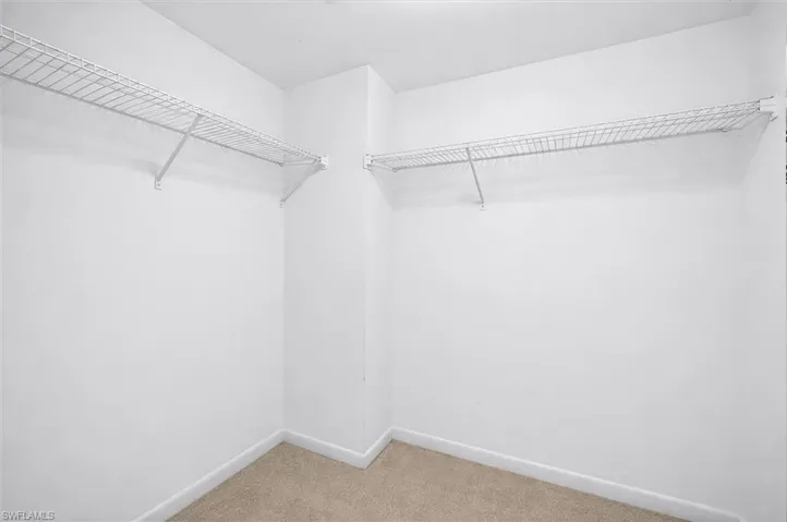Spacious walk-in closet featuring white wire shelving, white walls, and neutral carpeting