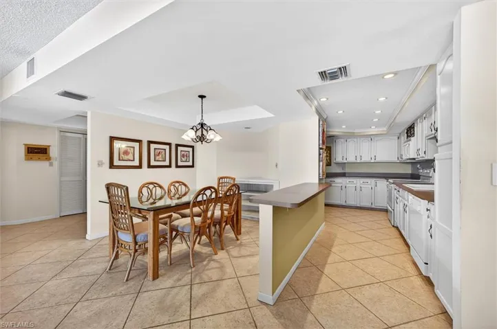 Spacious open-concept kitchen and dining area featuring tile flooring, white cabinetry, recessed lighting, and a breakfast bar