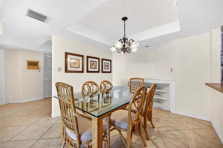 Dining area featuring tile flooring, a tray ceiling with a chandelier, and built-in shelving