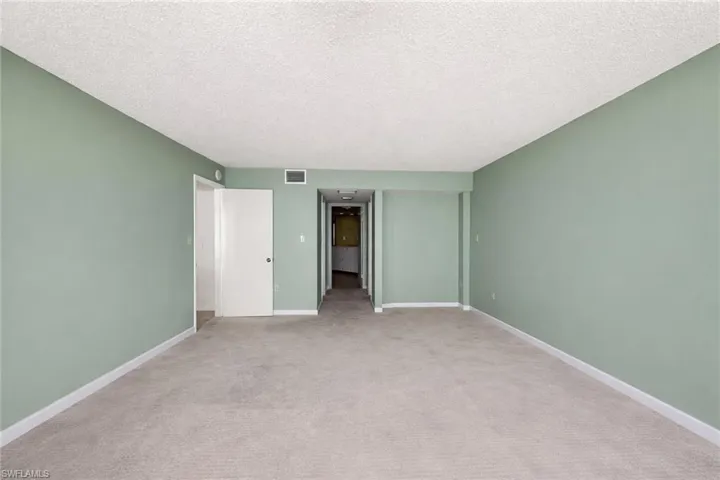 Spacious room with light green walls, neutral carpet, white baseboards, and a textured white ceiling