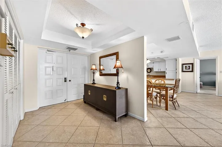 Entry foyer featuring light-toned tile flooring, white double entry doors, a tray ceiling with a semi-flush mount light fixture, and louvered bifold doors