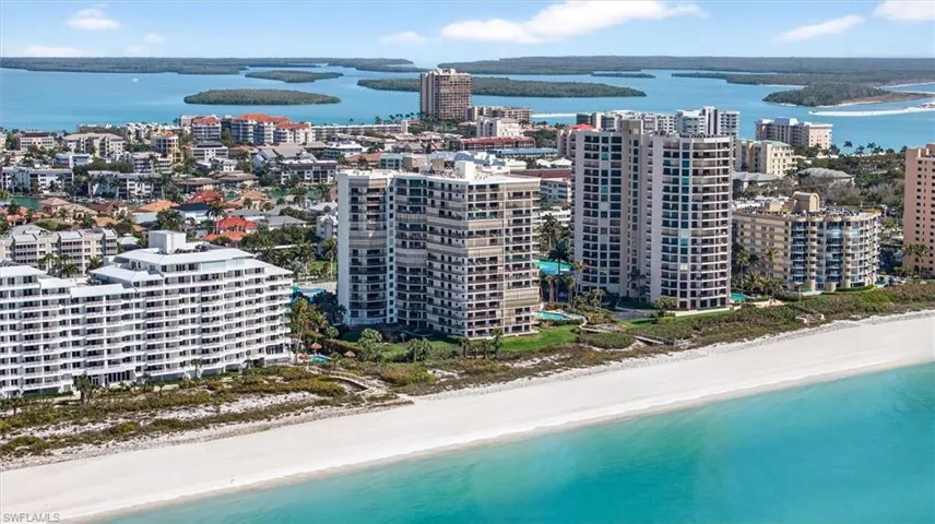 Coastal high-rise residences with private balconies overlooking a white sand beach and turquoise waters
