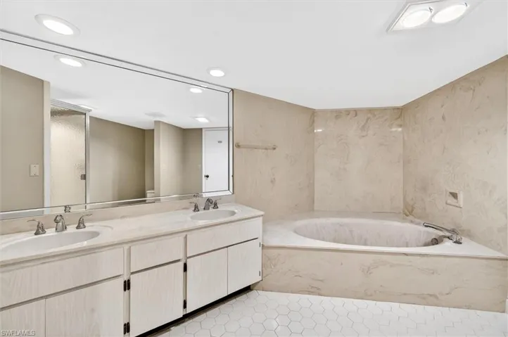 Bathroom featuring a built-in corner soaking tub, a double vanity with integrated sinks, and white hexagonal floor tiles