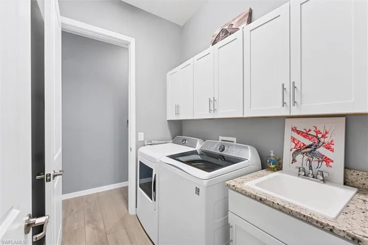 Laundry area with cabinets, sink, washer and clothes dryer, and light wood-type flooring