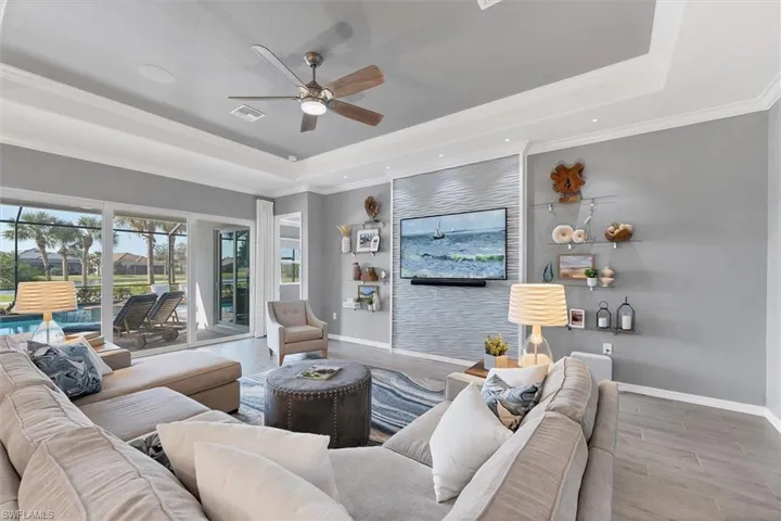 Living room with a raised ceiling, wood-type flooring, ceiling fan, and crown molding