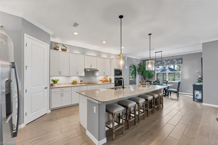 Kitchen with hanging light fixtures, a center island with sink, stainless steel appliances, light stone countertops, and white cabinets