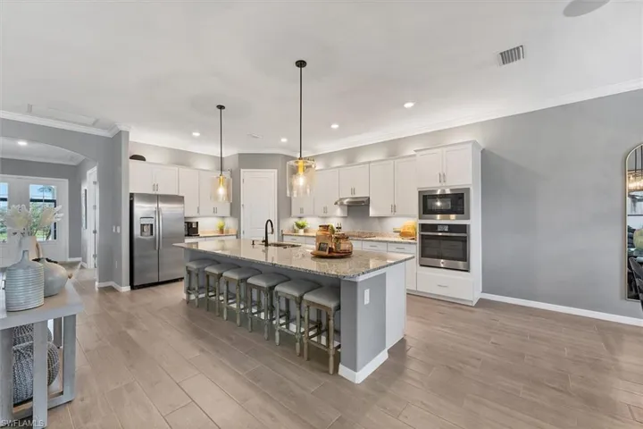 Kitchen featuring sink, white cabinets, light stone counters, stainless steel appliances, and a center island with sink