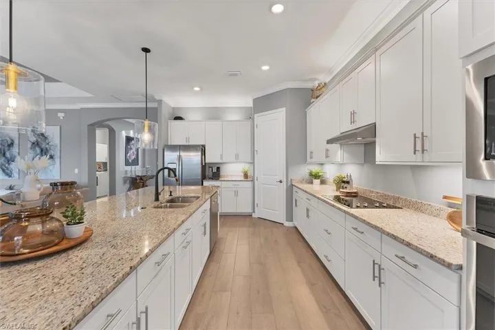 Kitchen featuring stainless steel appliances, white cabinetry, hanging light fixtures, and sink
