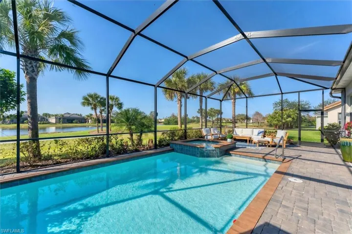 View of pool with an in ground hot tub, a water view, glass enclosure, and a patio area