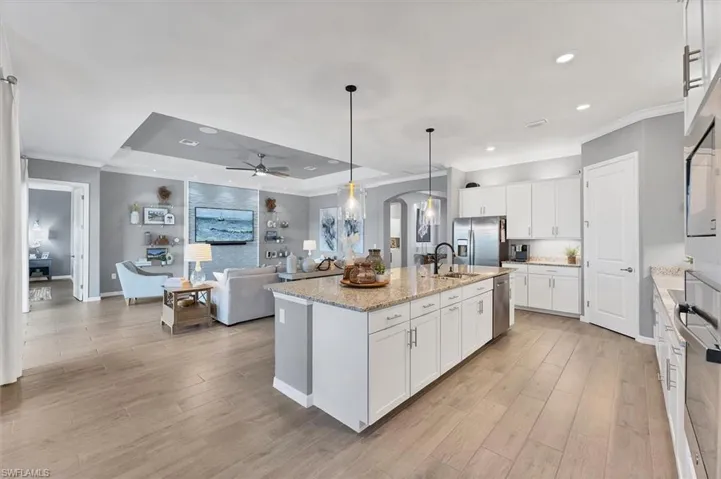 Kitchen featuring appliances with stainless steel finishes, pendant lighting, sink, white cabinets, and a kitchen island with sink