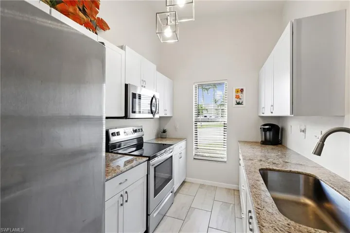 Kitchen featuring light stone countertops, white cabinetry, appliances with stainless steel finishes, and sink