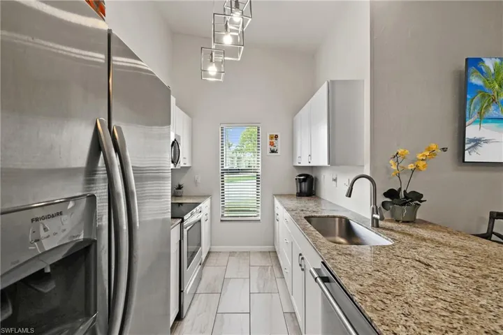 Kitchen featuring sink, white cabinetry, decorative light fixtures, appliances with stainless steel finishes, and light stone countertops