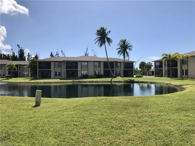 Waterfront condominium building with screened lanais, mature palm trees, and an expansive manicured lawn
