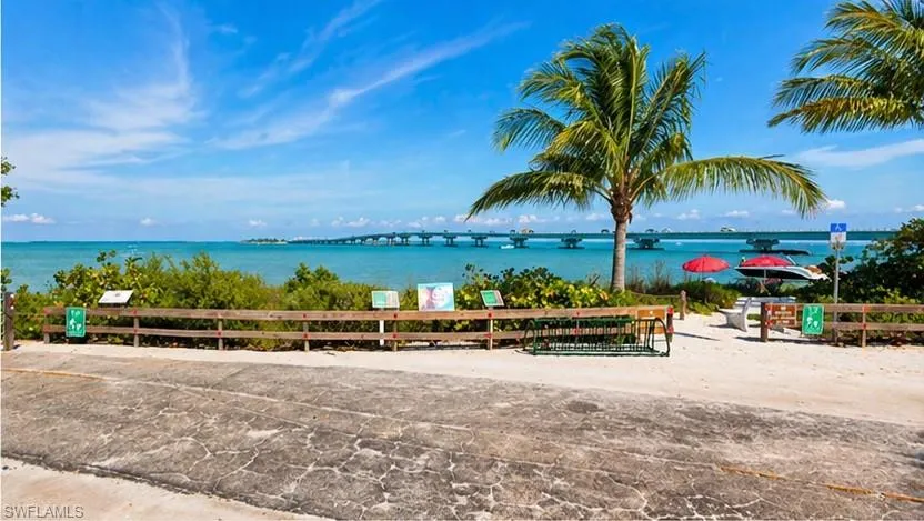 Waterfront setting featuring a distant bridge, mature palm trees, and a wooden fence bordering the water's edge