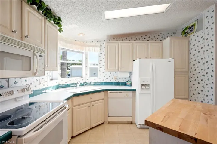 Kitchen featuring a sink, wallpapered walls, white appliances, and a textured ceiling