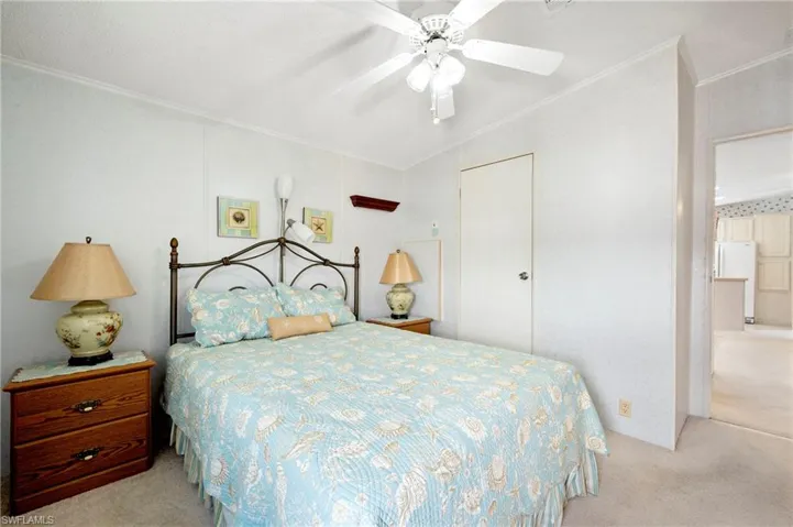 Bedroom with a ceiling fan, freestanding refrigerator, ornamental molding, and carpet