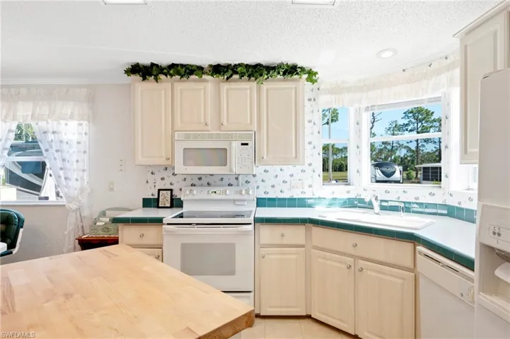 Kitchen featuring a sink, tile counters, white appliances, and a textured ceiling