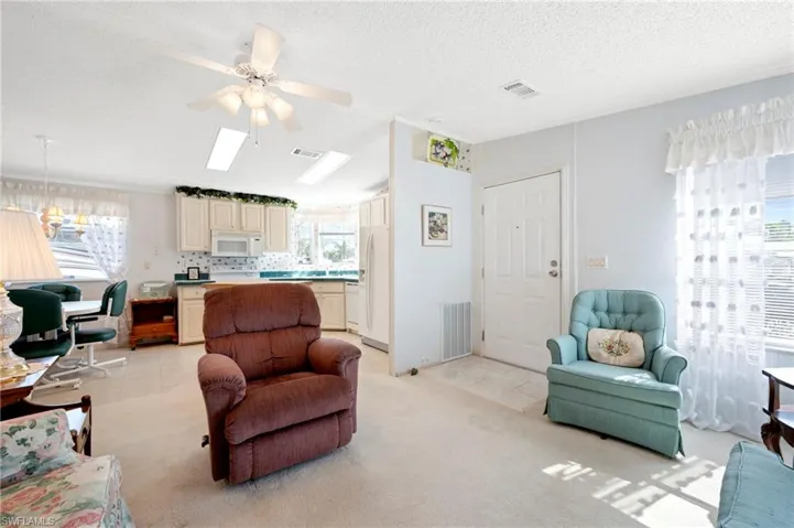 Living area featuring light carpet, visible vents, a textured ceiling, and ceiling fan