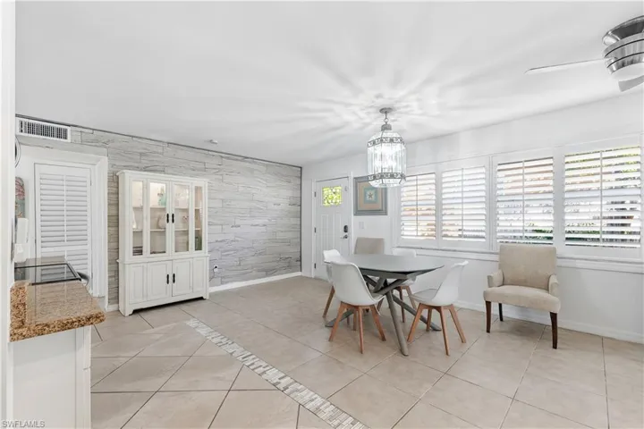 Dining area with light tile patterned flooring, plenty of natural light, an accent wall, and a chandelier