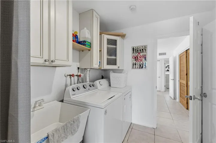 Laundry area featuring light tile patterned floors, separate washer and dryer, and cabinet space