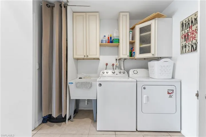 Washroom featuring cabinet space, light tile patterned flooring, and washer and clothes dryer