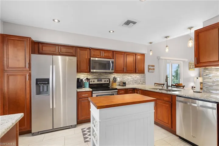 Kitchen featuring backsplash, appliances with stainless steel finishes, light stone countertops, decorative light fixtures, and brown cabinetry
